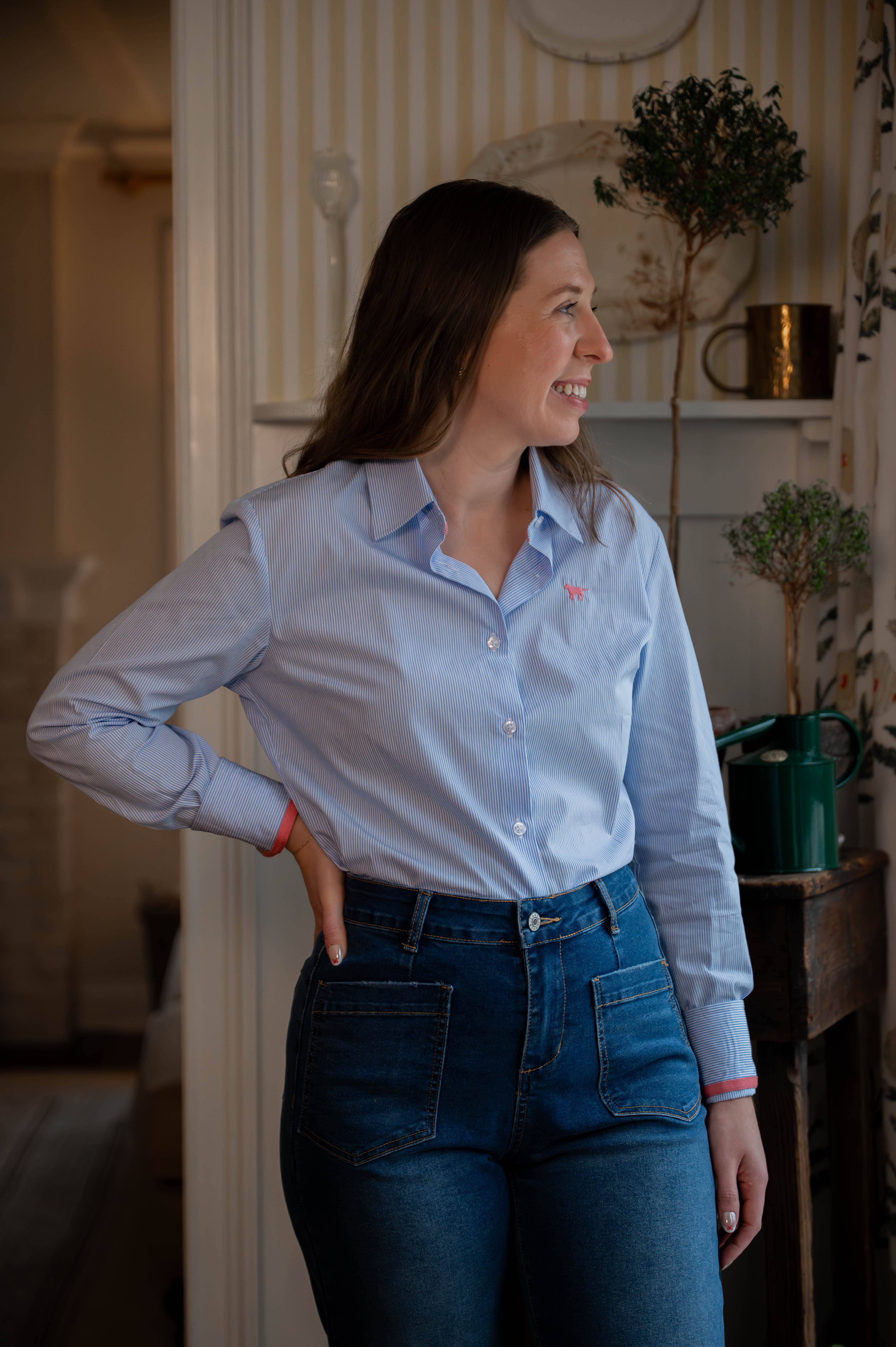 Woman wearing a light blue stripe shirt and jeans standing in a room with decor elements.